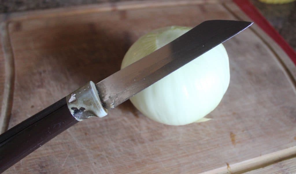 Knife with onion to be sliced up. - Missing the Disney parks? This Cheeseburger Egg Roll recipe is EASY and is a little taste of Disney you can make at home for your family! This easy recipe is the perfect appetizer or dinner recipe kids are sure to enjoy while parents will love them too! #Recipe 